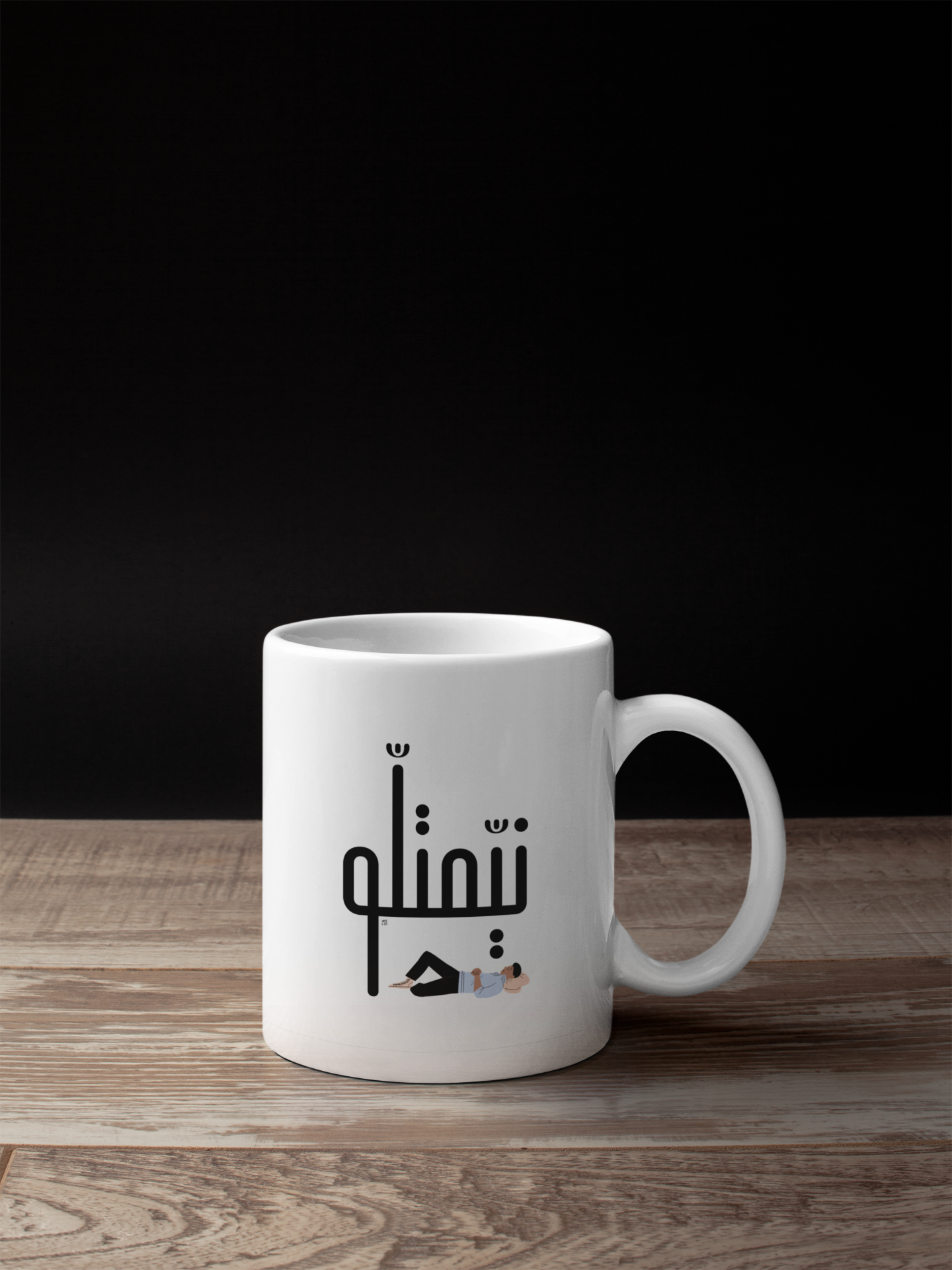 White ceramic mug with Arabic text and person relaxing illustration on wooden table
