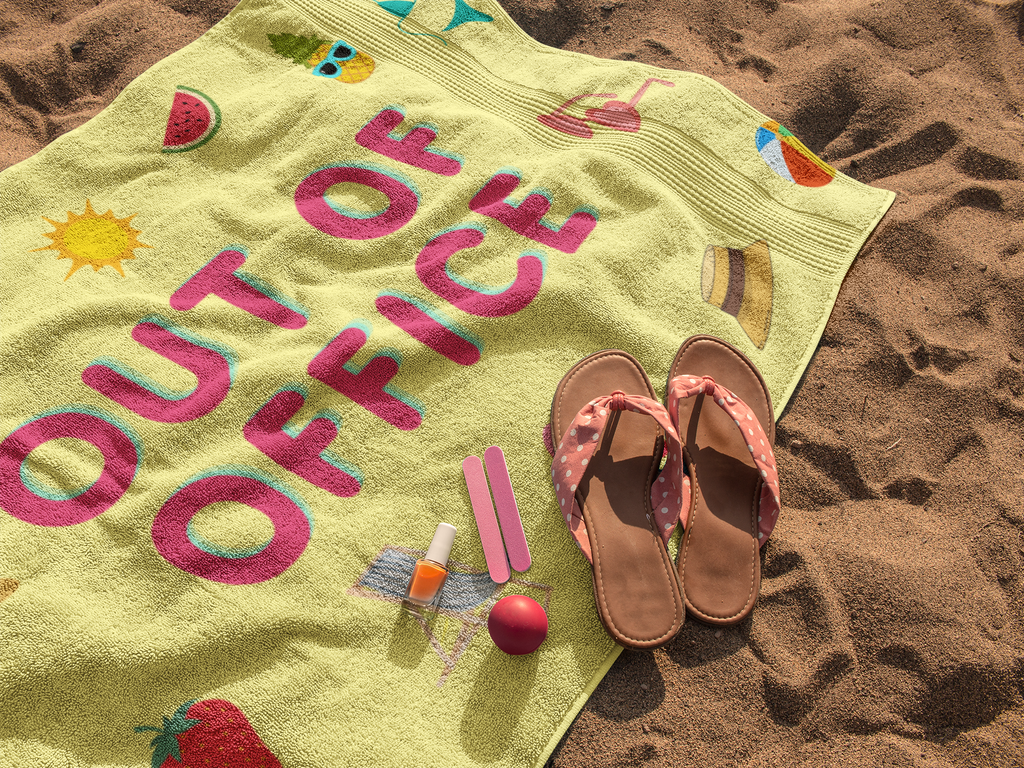 Yellow microfiber beach towel with 'Out of Office' text and summer icons, styled with pink sandals, nail polish, and beach accessories on sand.