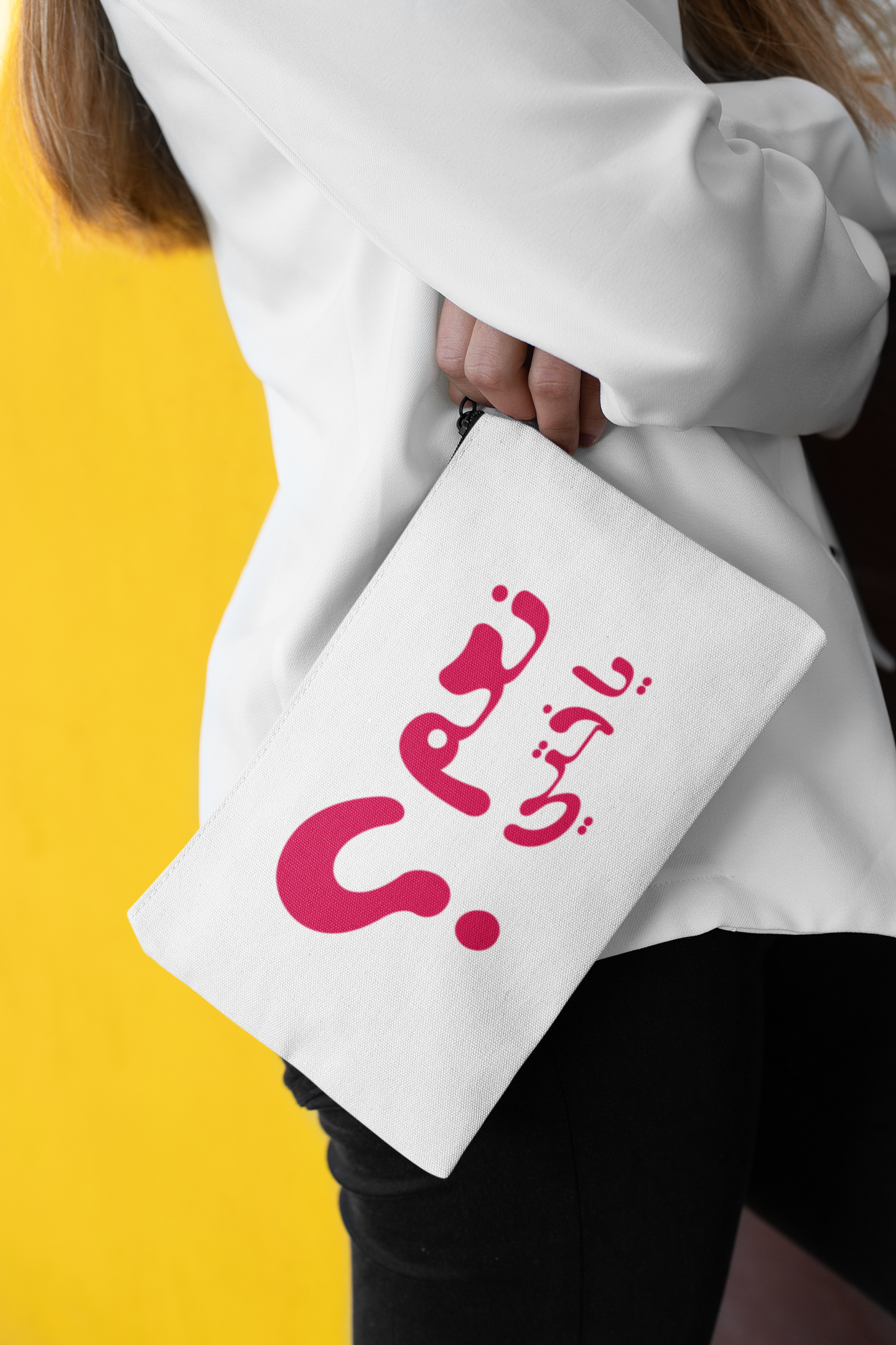 Person holding a white pouch with pink Arabic text against a yellow background