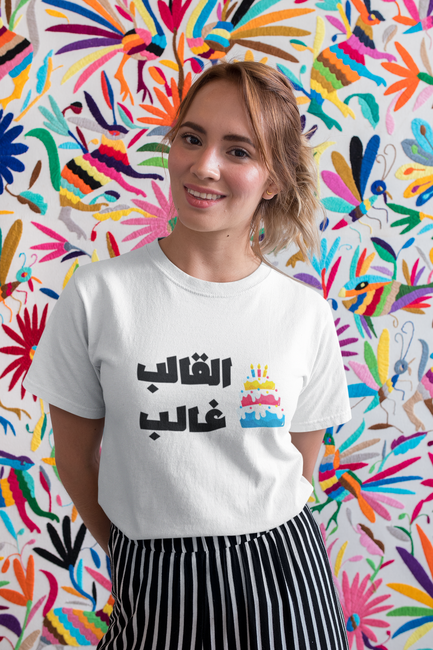 Woman wearing white T-shirt with Arabic text “القالب غالب” and birthday cake graphic