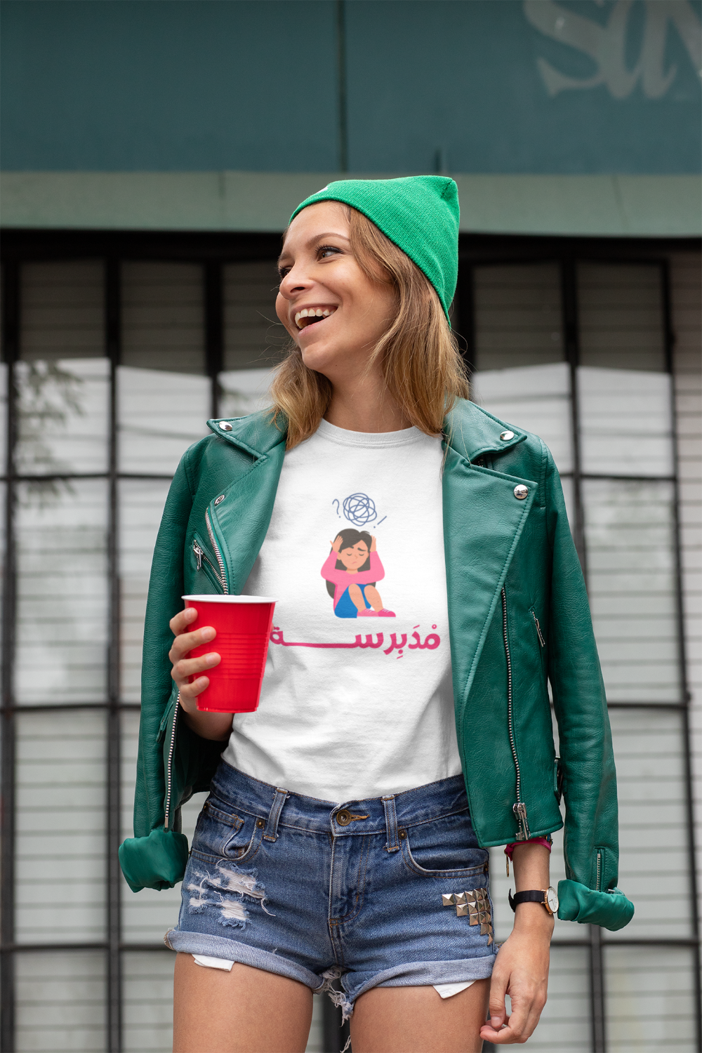 t shirt with arabic text with a woman dressed in green jacket and a denim shorts