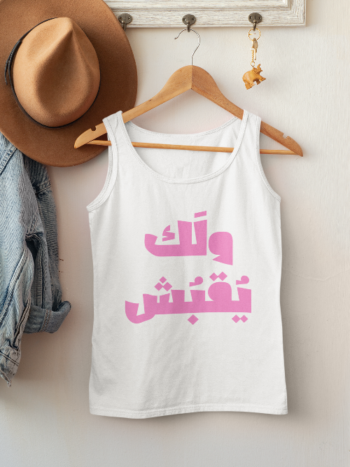 White tank top with pink Arabic text on a hanger against a white wall.
