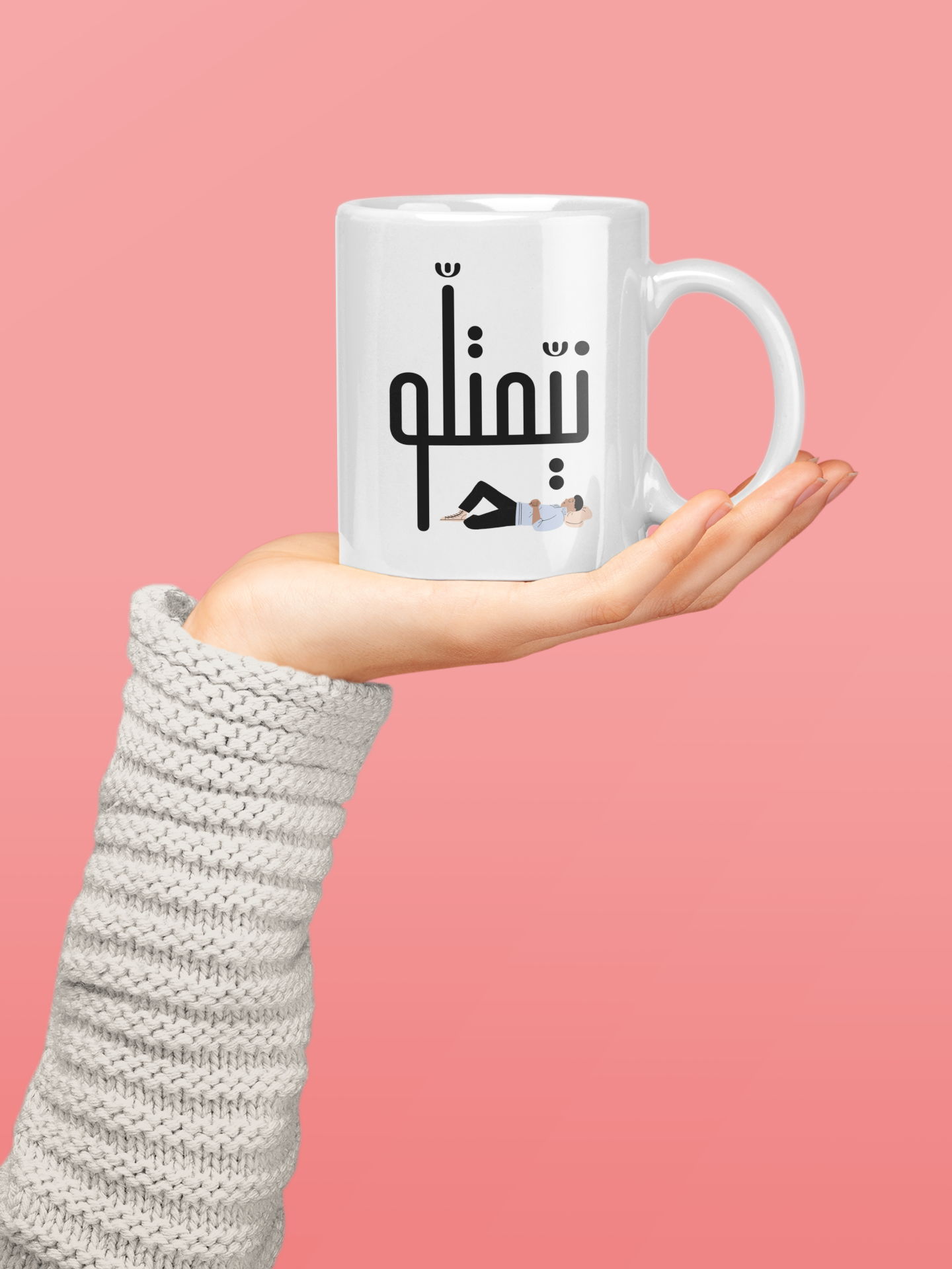 White ceramic mug with Arabic text held in a hand, pink background