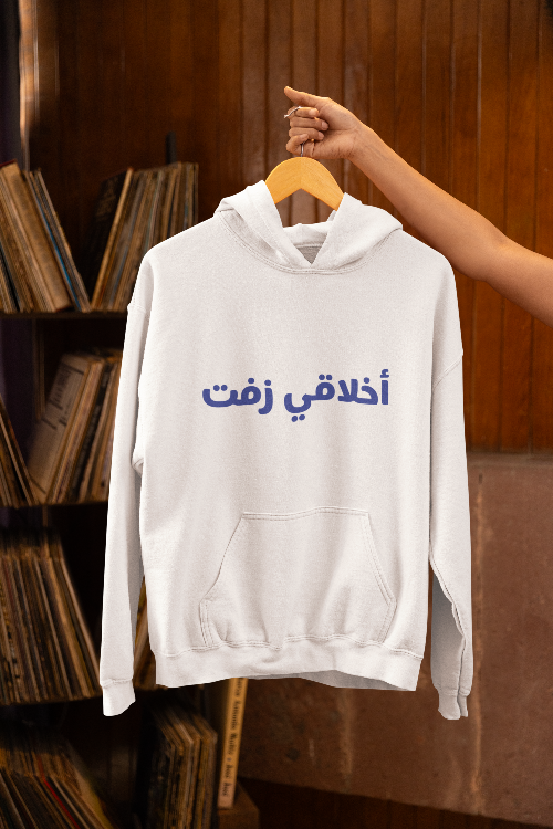 White hoodie with Arabic text on a wooden hanger against a wooden background