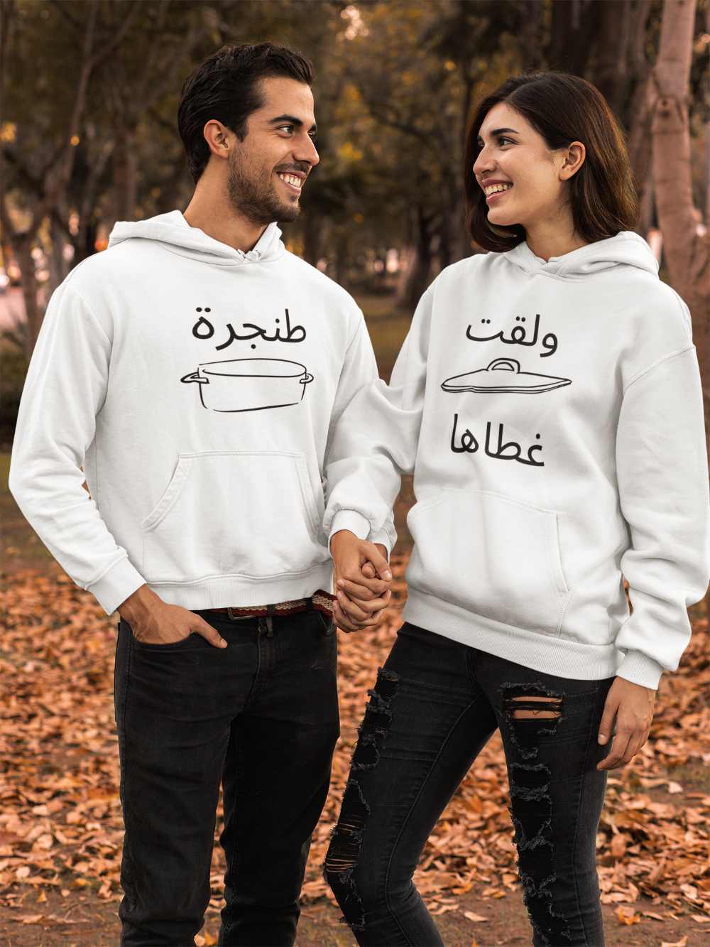 Two people wearing white hoodies with Arabic text and graphics, standing outdoors.
