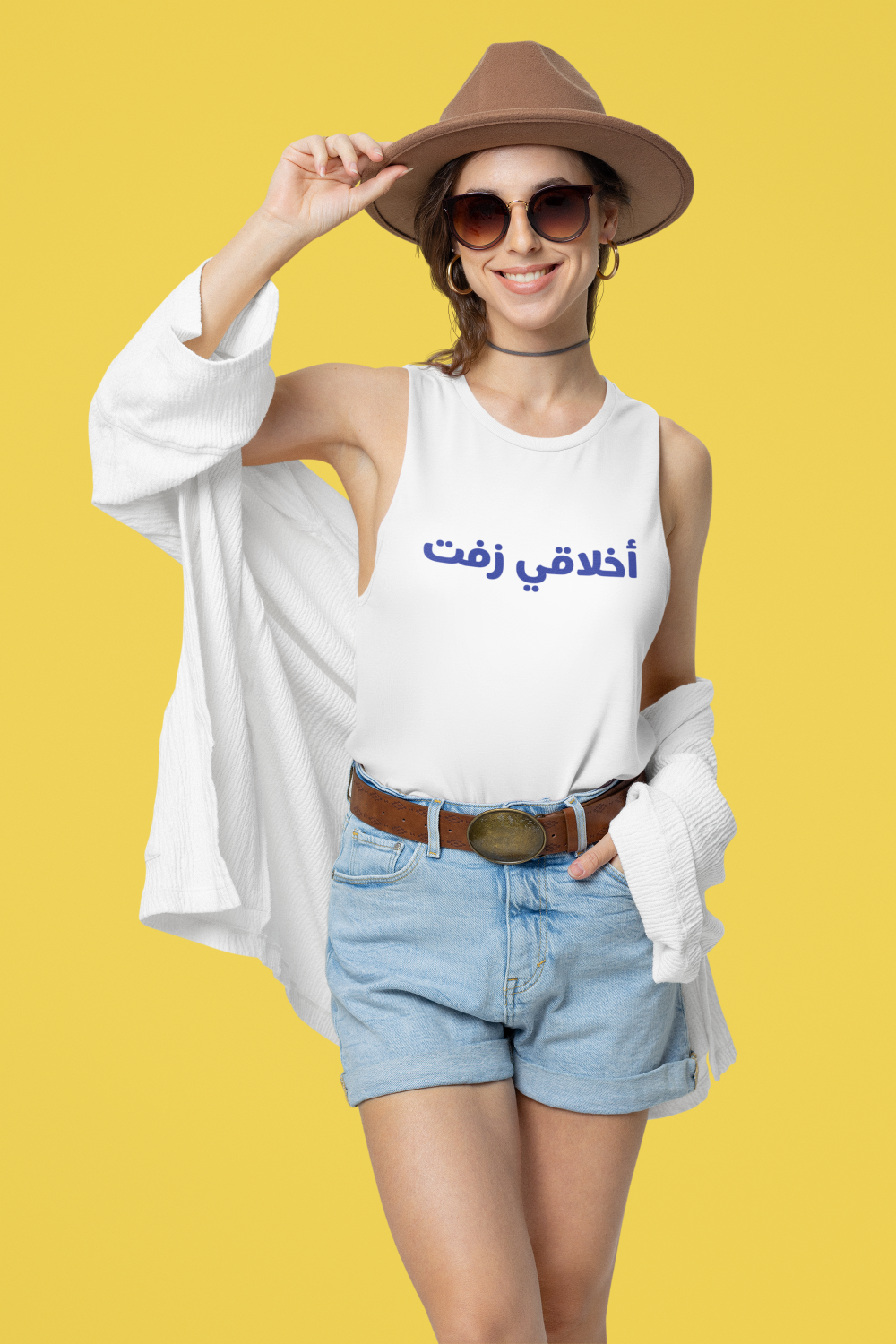 Woman wearing a white sleeveless shirt with Arabic text, denim shorts, and a brown hat on a yellow background