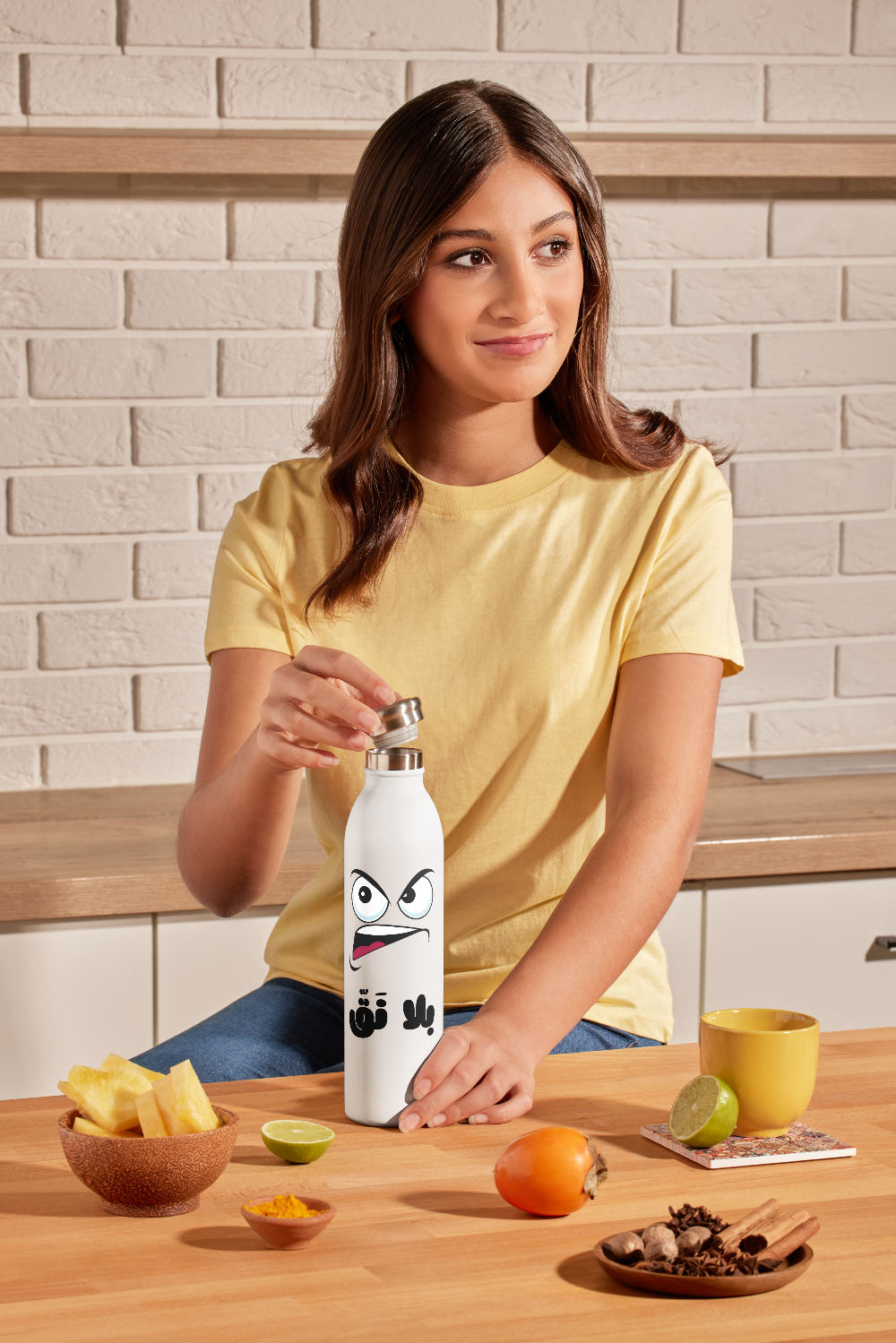 Woman holding a white water bottle with a face design in a kitchen setting
